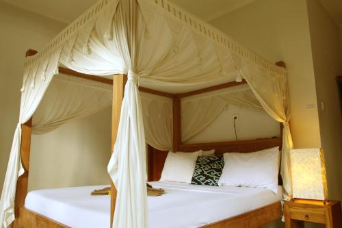 a bedroom with a canopy bed with white pillows at Suryadina Guest House in Ubud