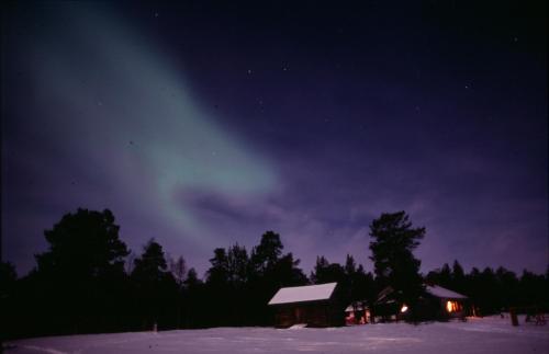 una baita nella neve di notte con l'aurora boreale di Ahkula House a Lemmenjoki