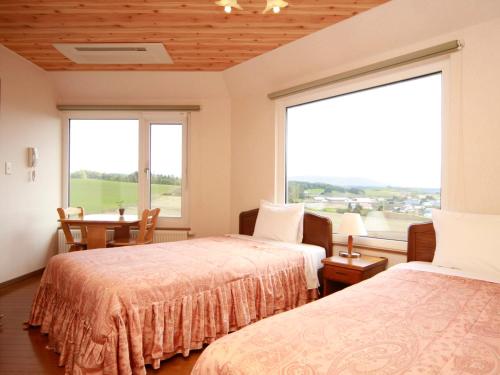 a room with two beds and a table and two windows at Pension Landscape Furano in Kami-furano