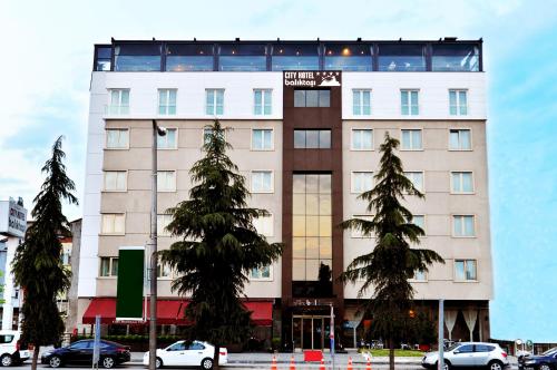 a tall white building with trees in front of it at Baliktasi City Hotel & Spa in Ordu