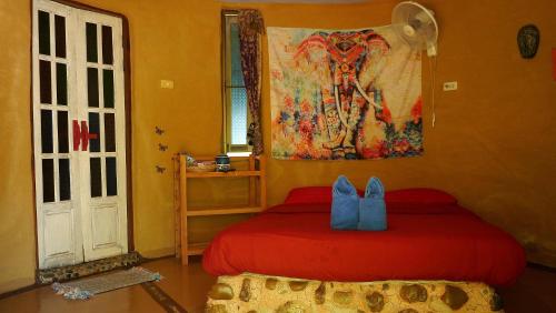 Un dormitorio con una cama roja y una pintura en la pared en Pho Rak Nah Pai, en Pai
