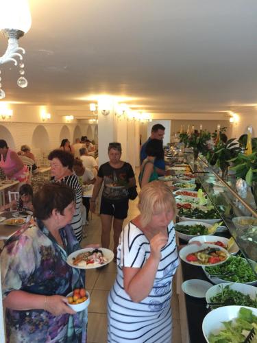 Olimpos Beach Hotel by RRH&R في كيمير: مجموعة من الناس تقف حول خط بوفيه مع أطباق من الطعام