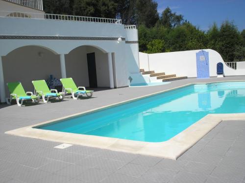 a swimming pool with green chairs and a house at Vivenda Pirilampo in Vila Nova de Poiares