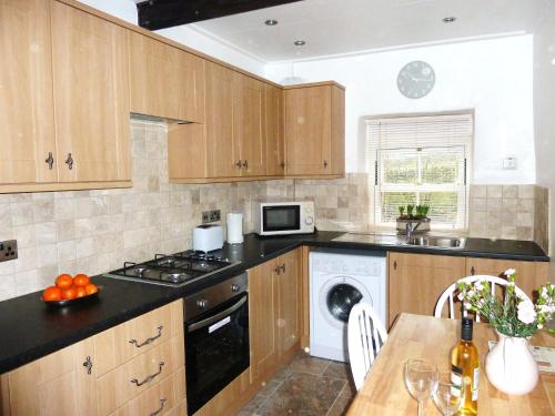 a kitchen with wooden cabinets and a washer and dryer at Holme House Cottage in Oakworth