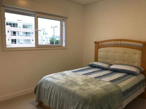 um quarto com uma cama com duas almofadas e uma janela em Apto Praia Ingleses 3q 2g em Florianópolis