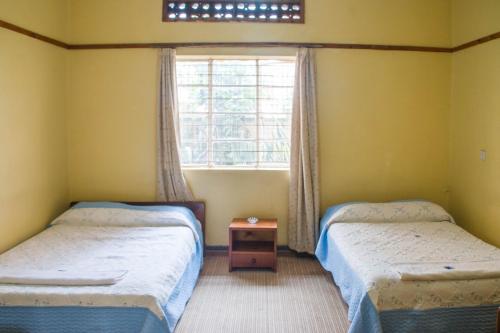 two twin beds in a room with a window at Pelikan Hotel in Mbarara