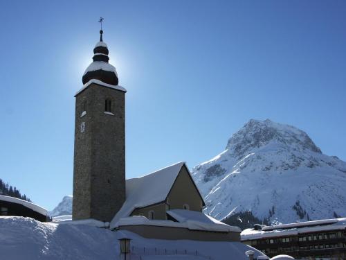 a building with a clock tower with a snow covered mountain at Pension Kilian in Lech am Arlberg