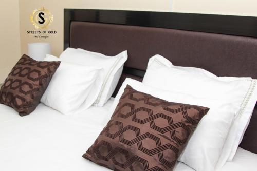 a bed with white pillows and brown and white pillows at Streets of Gold Guest House in Gaborone