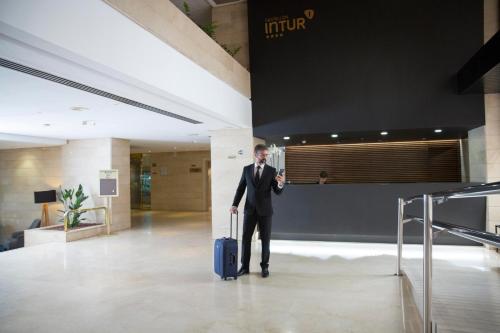 a man in a suit with a suitcase in a lobby at Intelier Rosa in Castellón de la Plana
