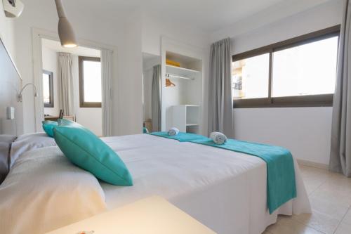 a white bedroom with a large bed with blue pillows at Hotel Orosol by Typic Hotels in San Antonio