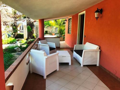 a porch with white chairs and an orange wall at Hotel Village Eden in Capo Vaticano