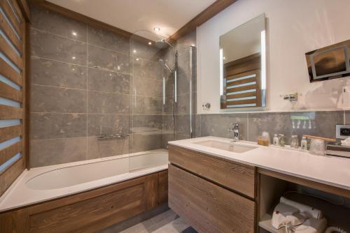 a bathroom with a tub and a sink and a mirror at Hotel le Petit Dru in Morzine