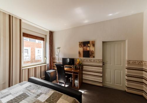 a bedroom with a bed and a desk and a window at City Hotel Stolberg in Stolberg