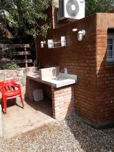 una cocina de ladrillo con fregadero y silla roja en Cabañas Doña Itati, en Villa Carlos Paz