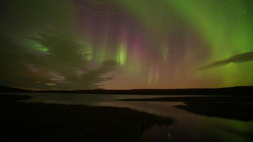 an aurora over a body of water at night at Osman Kelohovi in Utsjoki