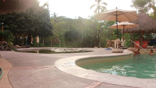 a swimming pool with an umbrella and people in it at Casa Del Sol in Lo de Marcos