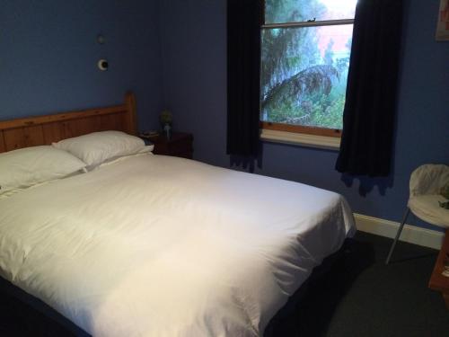 1 dormitorio con cama blanca y ventana en Tramway Cottage, en Strahan