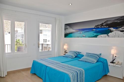 Un dormitorio con una cama azul con una pintura en la pared en Hotel Capri, en Puerto Pollensa