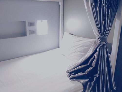 a bed with a blue curtain next to a window at The August Hostel in Chiang Mai