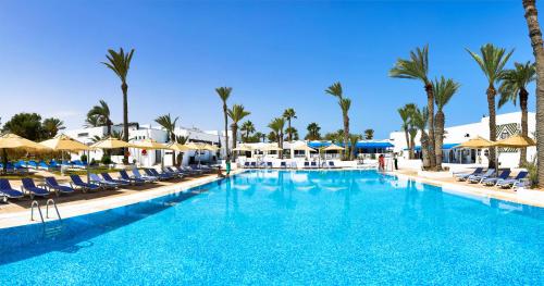 a large swimming pool with chairs and palm trees at Hari Club Beach Resort in Aghīr