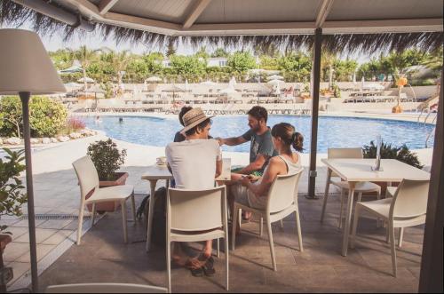 een groep mensen aan een tafel bij een zwembad bij Camping Sènia Tucan in Lloret de Mar