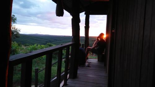 a woman sitting on the porch of a cabin with the sunset at Tree Trails Homestay & Offers Jungle Trekk-Scooter For Rental in Banlung