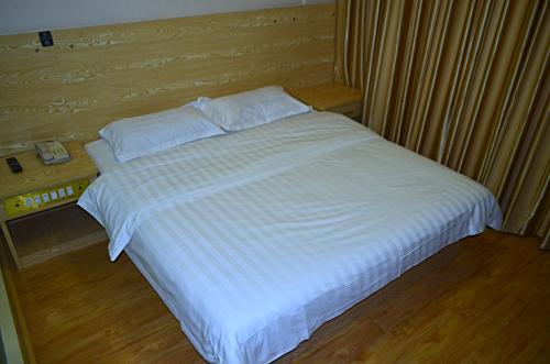 a bed with white sheets and pillows in a bedroom at JUNYI Hotel Shandong Qingdao Huangdao District Shiyou University in Xianlang