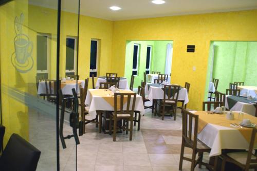 uma sala de jantar com mesas e cadeiras e paredes amarelas em Hotel Manayara em Campo Largo