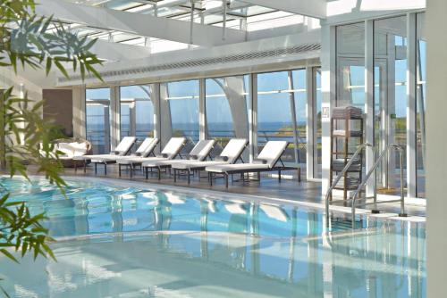 - une piscine avec des chaises longues blanches dans un bâtiment dans l'établissement Miramar La Cigale Hotel Thalasso & Spa, à Arzon