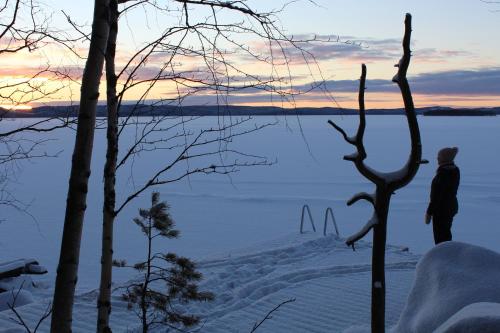 a person standing in the snow next to a body of water at Nukula Guestrooms in Oravasaari