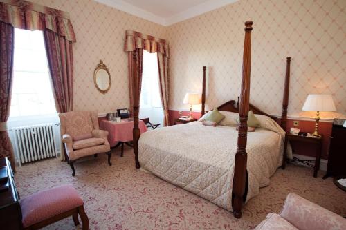 
a hotel room with a bed, chair, and nightstand at Culloden House Hotel in Inverness
