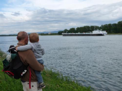 a man carrying a child on his back near a lake at Gîte du héron in La Wantzenau