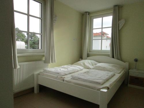 a white bed in a room with two windows at Haus Meeresblick Wohnung A 1.04 in Baabe