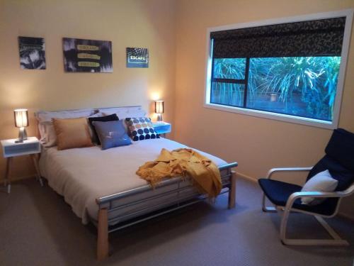 1 dormitorio con cama, ventana y silla en Dream Escape for 2 en Paraparaumu Beach