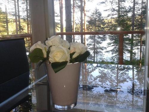 a vase with white roses sitting in front of a window at Pyhäjärven Lomakylä in Ruolahti
