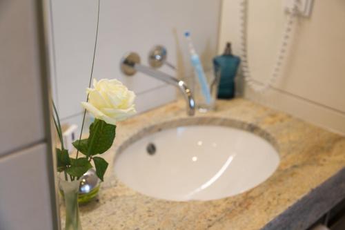 a bathroom sink with a white rose in a vase at Pfaffinger Hof in Pfaffing