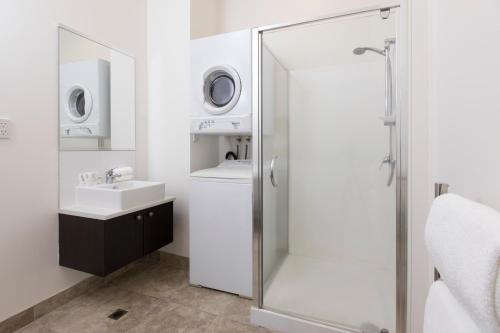 uma casa de banho com um chuveiro, um lavatório e uma máquina de lavar roupa em Quest Hamilton Serviced Apartments em Hamilton