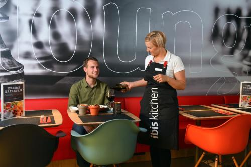 a woman in an apron standing next to a man in a restaurant at ibis Charleroi Airport Brussels South in Charleroi
