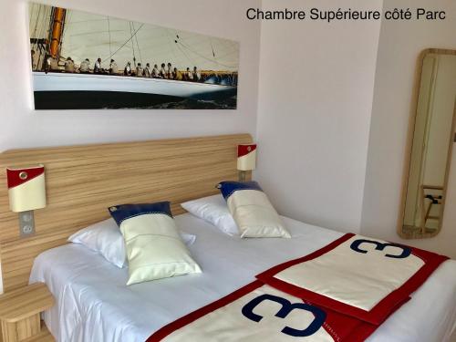a bedroom with a bed with white sheets and blue pillows at Hotel Club Le Plein Sud Vacances Bleues in Hyères