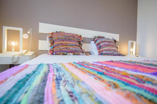 a bed with a multicolored blanket and pillows at Oasis Porto Grande in Mindelo