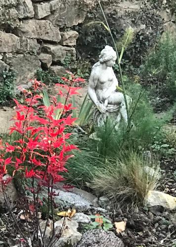 a statue sitting in a garden with red flowers at 116 Espigarie in Le Vigan