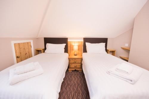 two beds in a room with white sheets at The Burley Inn in Burley