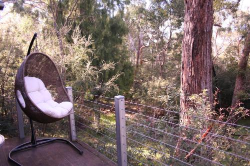 a wicker chair sitting on a deck in the woods at Heavenly Retreat in Halls Gap