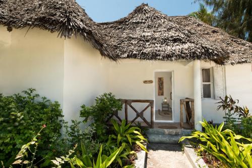 a small white house with a thatched roof at Driftwood Beach Lodge in Jambiani