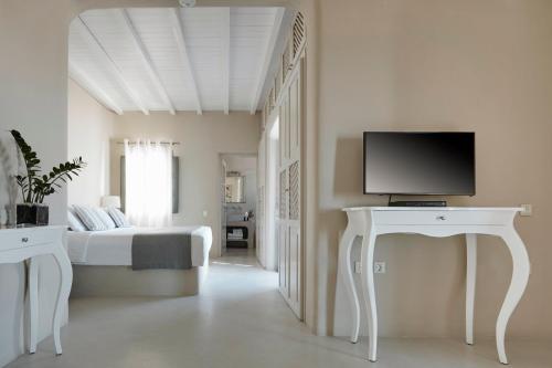 a white bedroom with a bed and a tv on a table at Carpe Diem Santorini in Pirgos