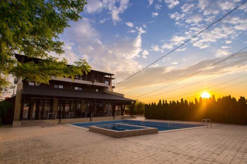 a building with a swimming pool in front of a sunset at Pensiunea Sara in Focşani