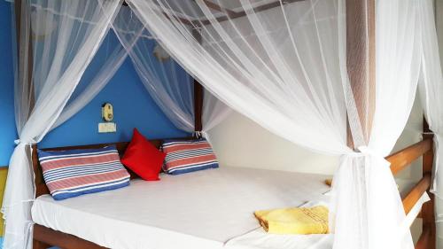 Una cama con cortinas blancas y almohadas coloridas. en Calidan, en Mirissa