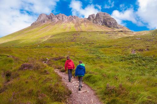 two people walking down a trail in front of a mountain at Harbour House in Ullapool
