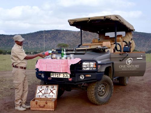 a man standing next to a vehicle with a picnic table at One Nature Nyaruswiga Serengeti in Banagi