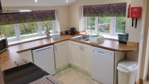 a kitchen with white cabinets and a sink and windows at Mallows Byre Yetminster in Sherborne